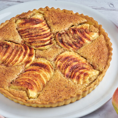 Teller mit Apfeltarte mit Frangipane und Zimt sowie Äpfeln daneben