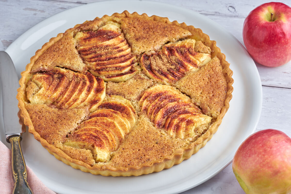 Teller mit Apfeltarte mit Frangipane und Zimt sowie Äpfeln daneben