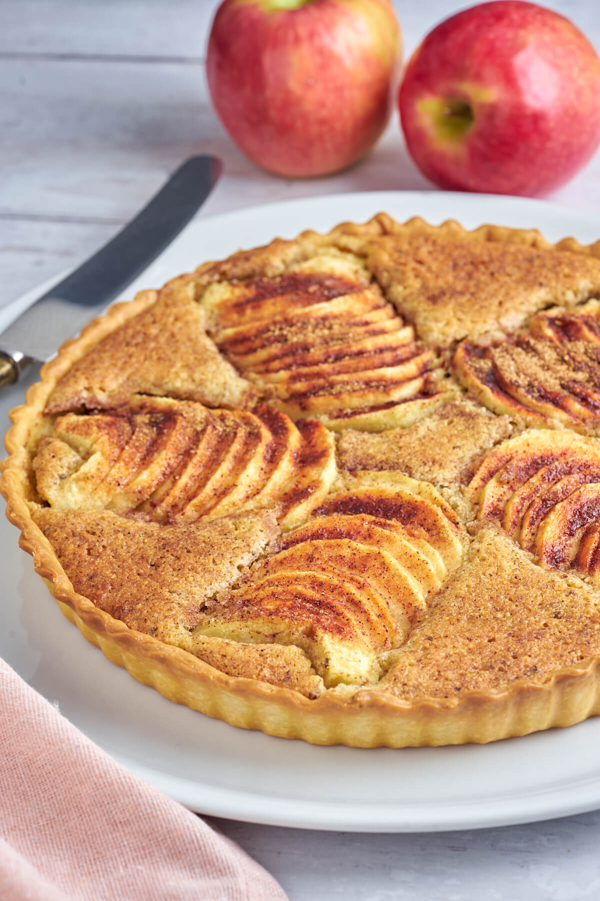 Apfeltarte mit Frangipane auf einem Teller mit Äpfeln und einem Messer